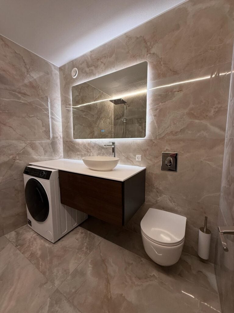 Lyst, moderne badeværelse med oplyst spejl og fritstående toilet.