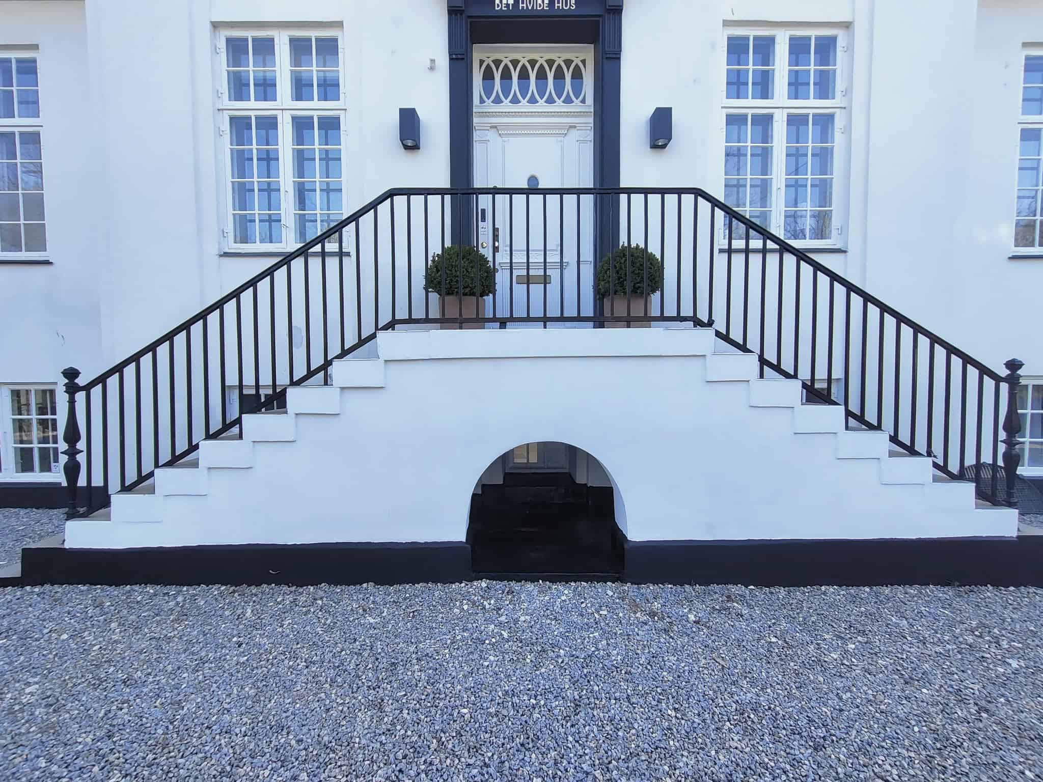 Facade på hvid murstensbygning i Holbæk med sort gelænder.