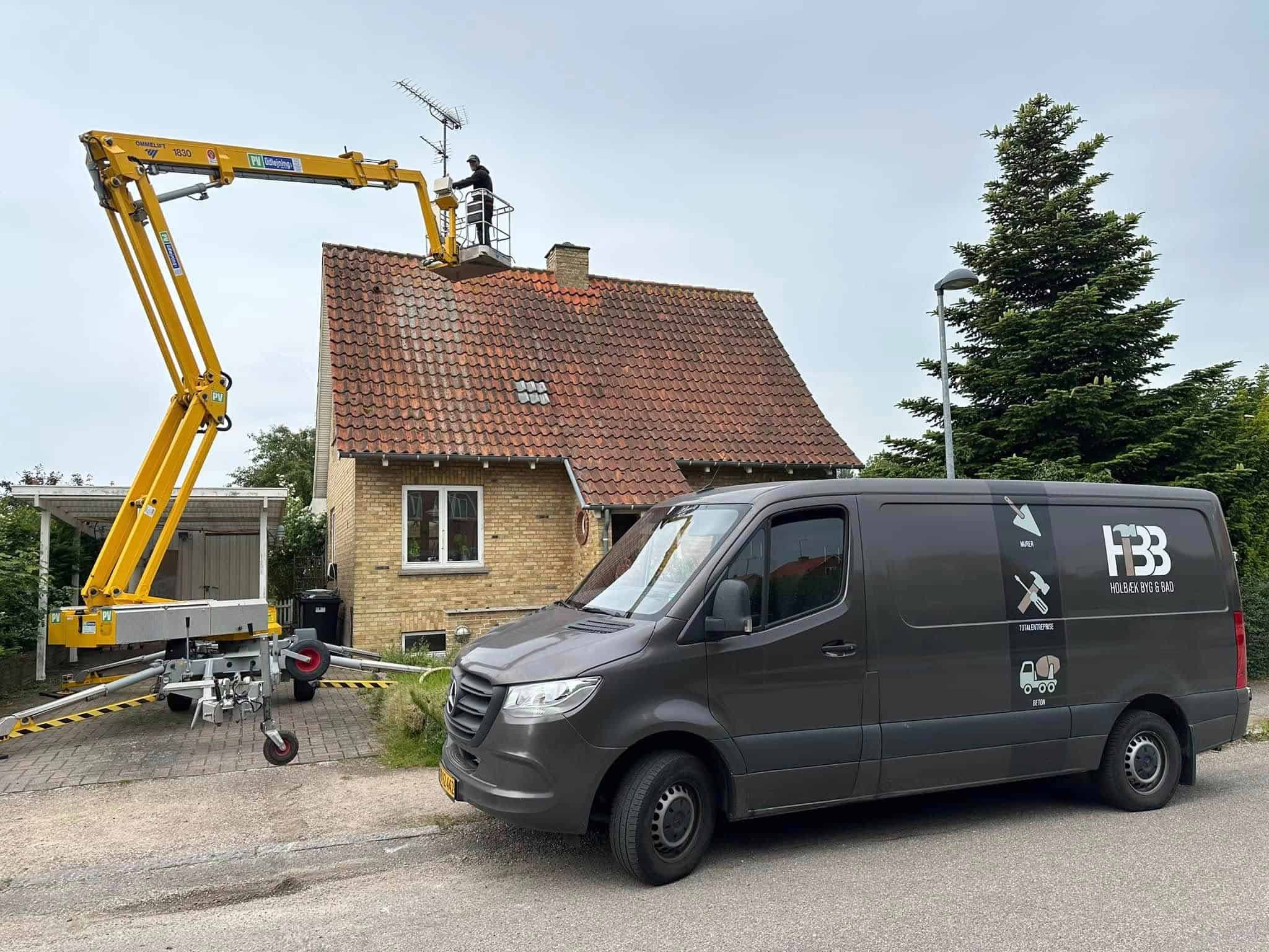Murer arbejder på renovering af tag, murerbil med logo i forgrunden.